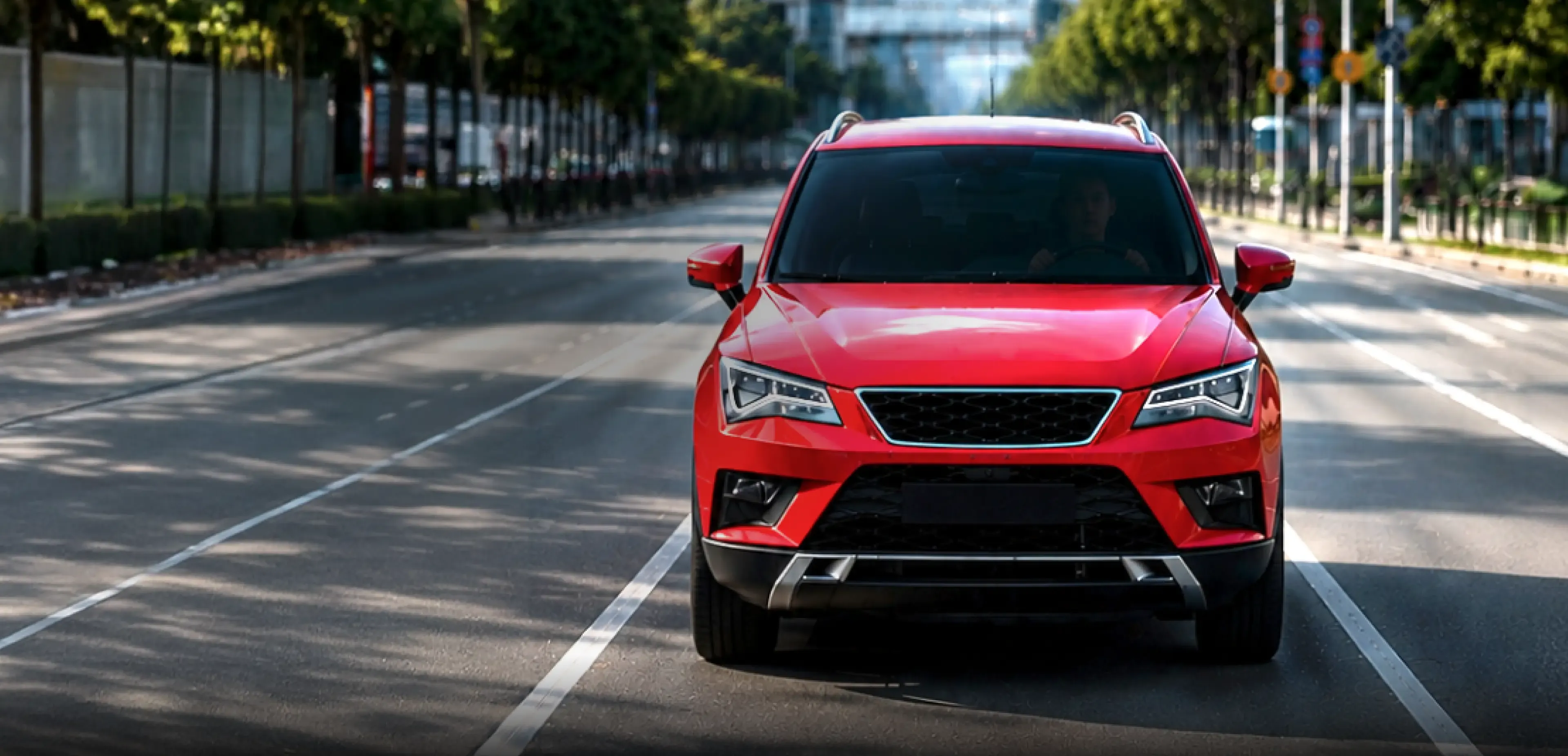 A red SUV driving on a tree-lined city road.