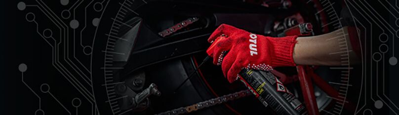 Dłoń w czerwonej rękawicy trzyma spray MOTUL przy motocyklowym napędzie